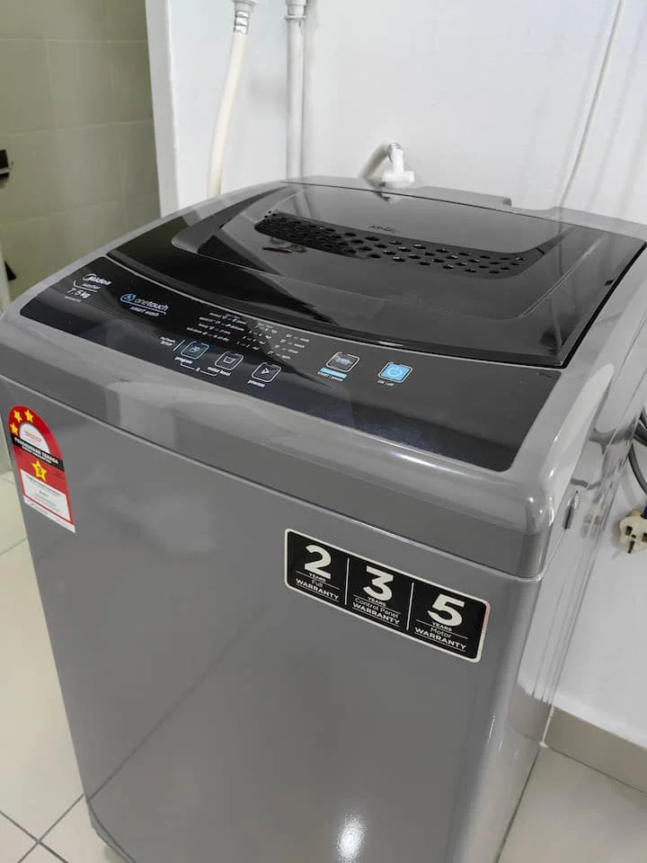 Laundry features: top-load washing machine in grey, control panel with digital display, water inlet hose, drain hose, tile flooring, white painted walls.